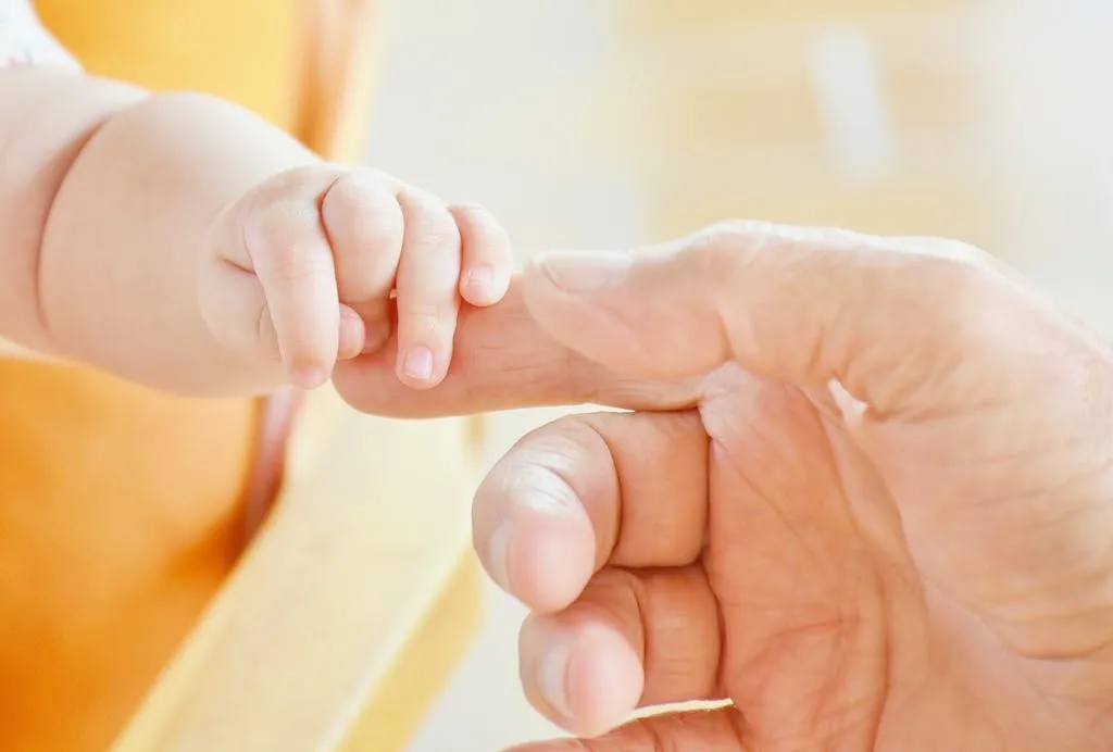 Close-up of a baby’s hand holding an adult’s finger, symbolizing parental love.
