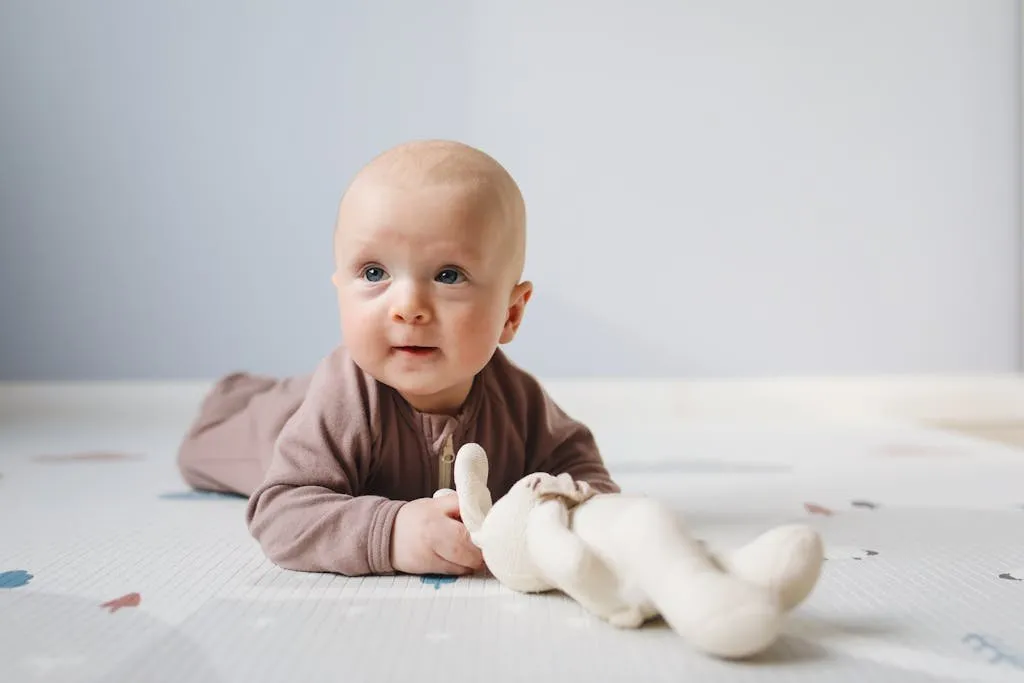 Cute baby on floor with stuffed toy, light indoor setting, focus on facial expression.