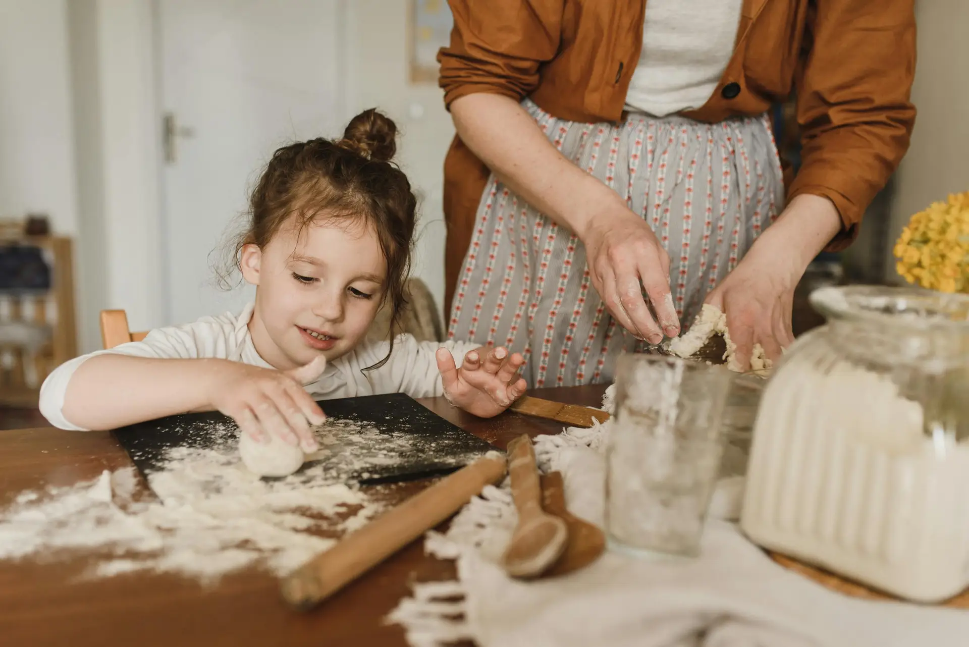 A young girl enjoys baking with an adult, kneading dough in a cozy kitchen.