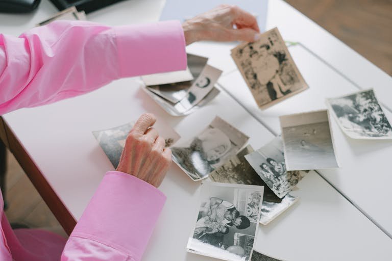 An elderly woman in a pink shirt sorting through old black and white family photographs, evoking nostalgia.