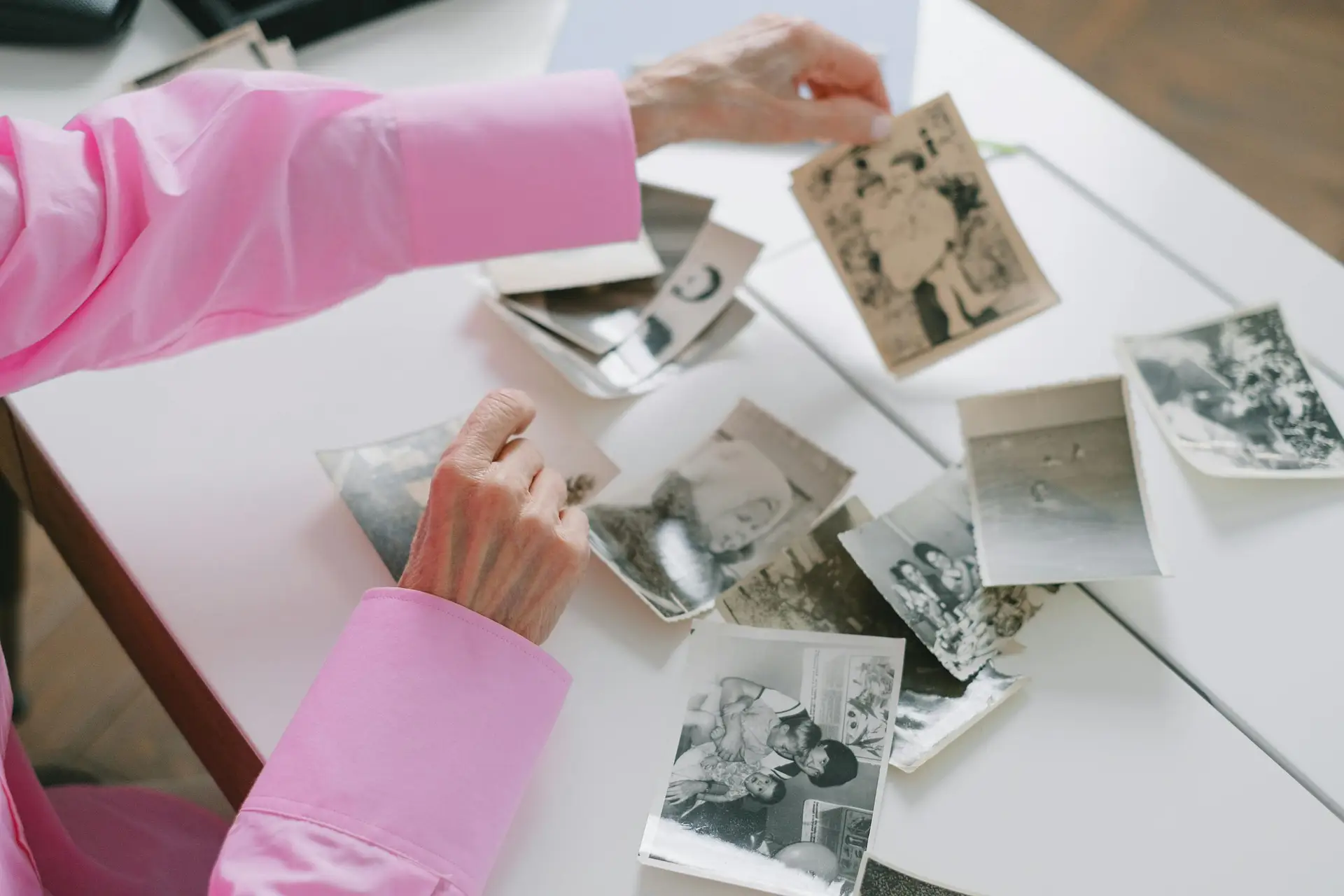 An elderly woman in a pink shirt sorting through old black and white family photographs, evoking nostalgia.