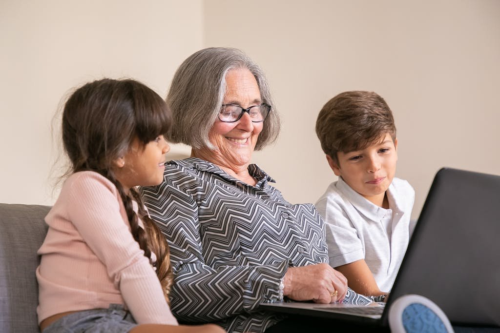 Cheerful grandmother bonding with grandchildren while using a laptop indoors.