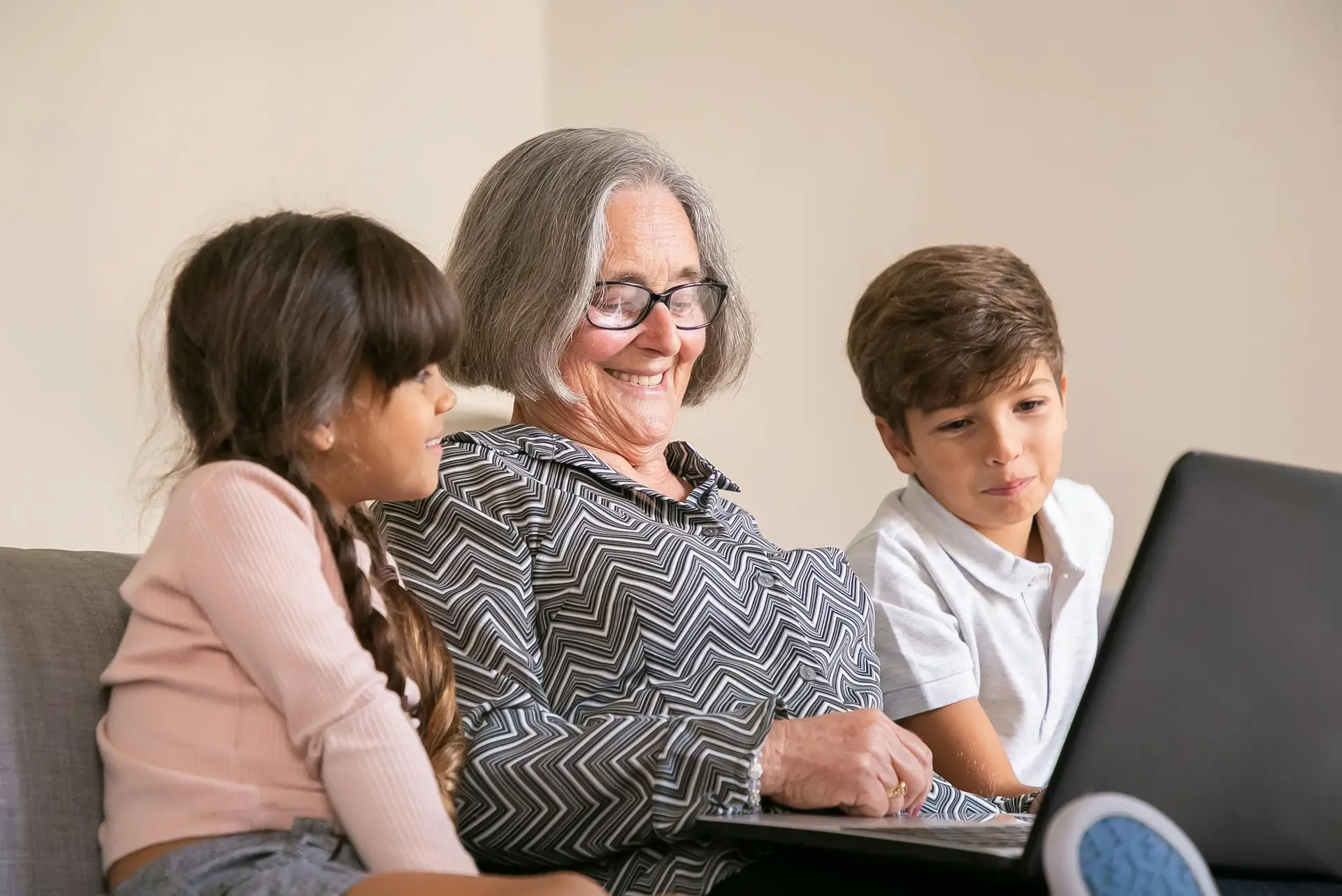 Cheerful grandmother bonding with grandchildren while using a laptop indoors.