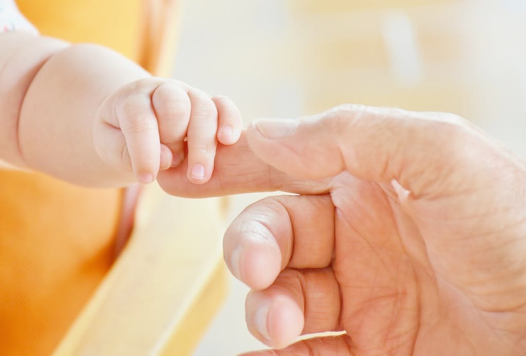 Close-up of a baby's hand holding an adult's finger, symbolizing parental love.