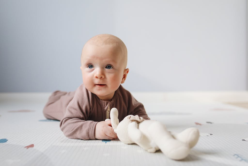 Cute baby on floor with stuffed toy, light indoor setting, focus on facial expression.